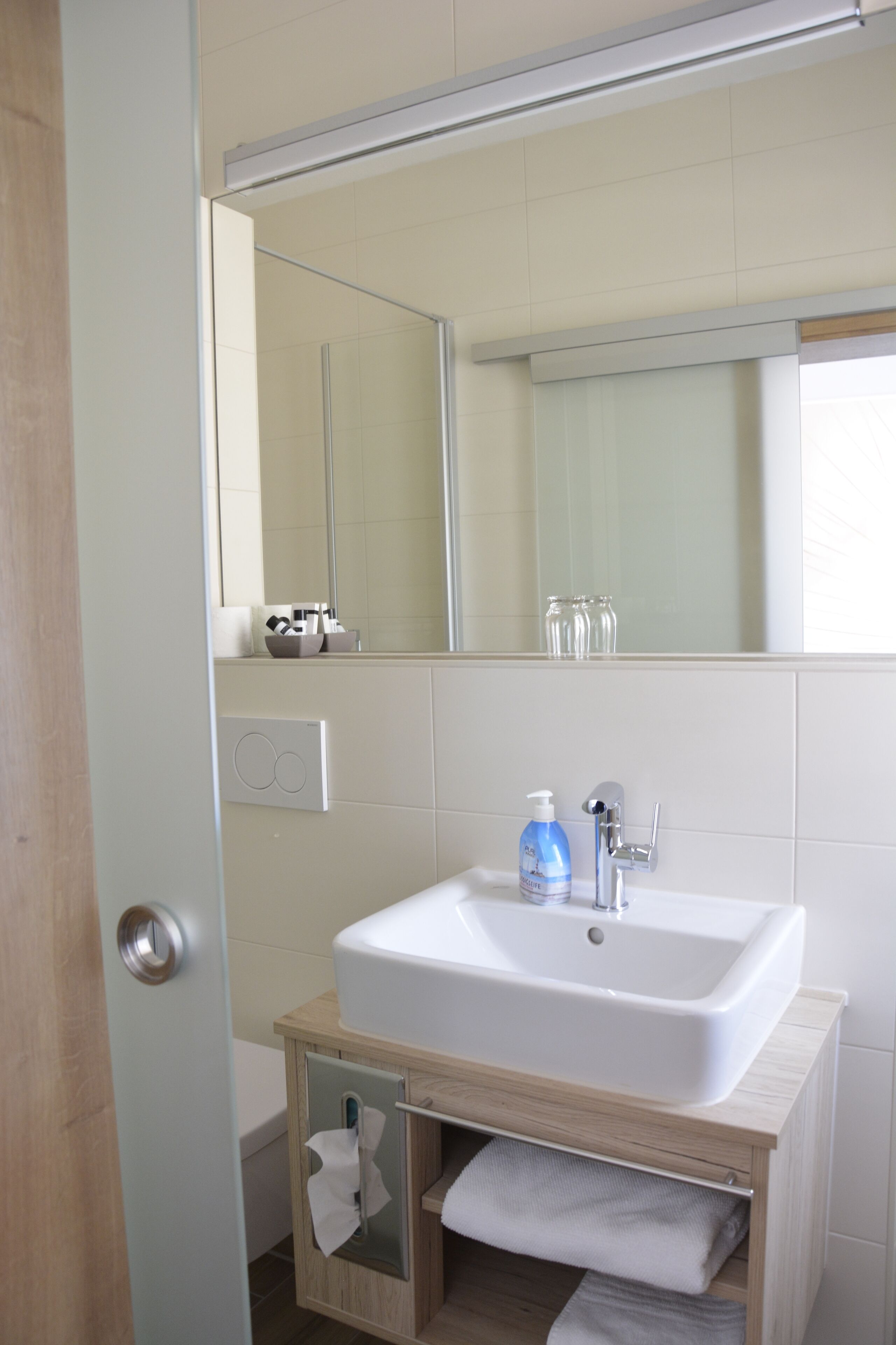 Un baño con lavamanos blanco, espejo y toallero.