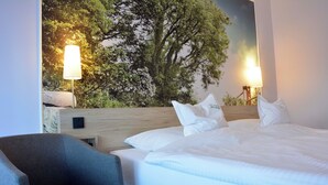 A hotel room with a large bed, two bedside lamps, a chair, and a wall mural of trees. - Hotel Restaurant Zur Post (Holdorf)
