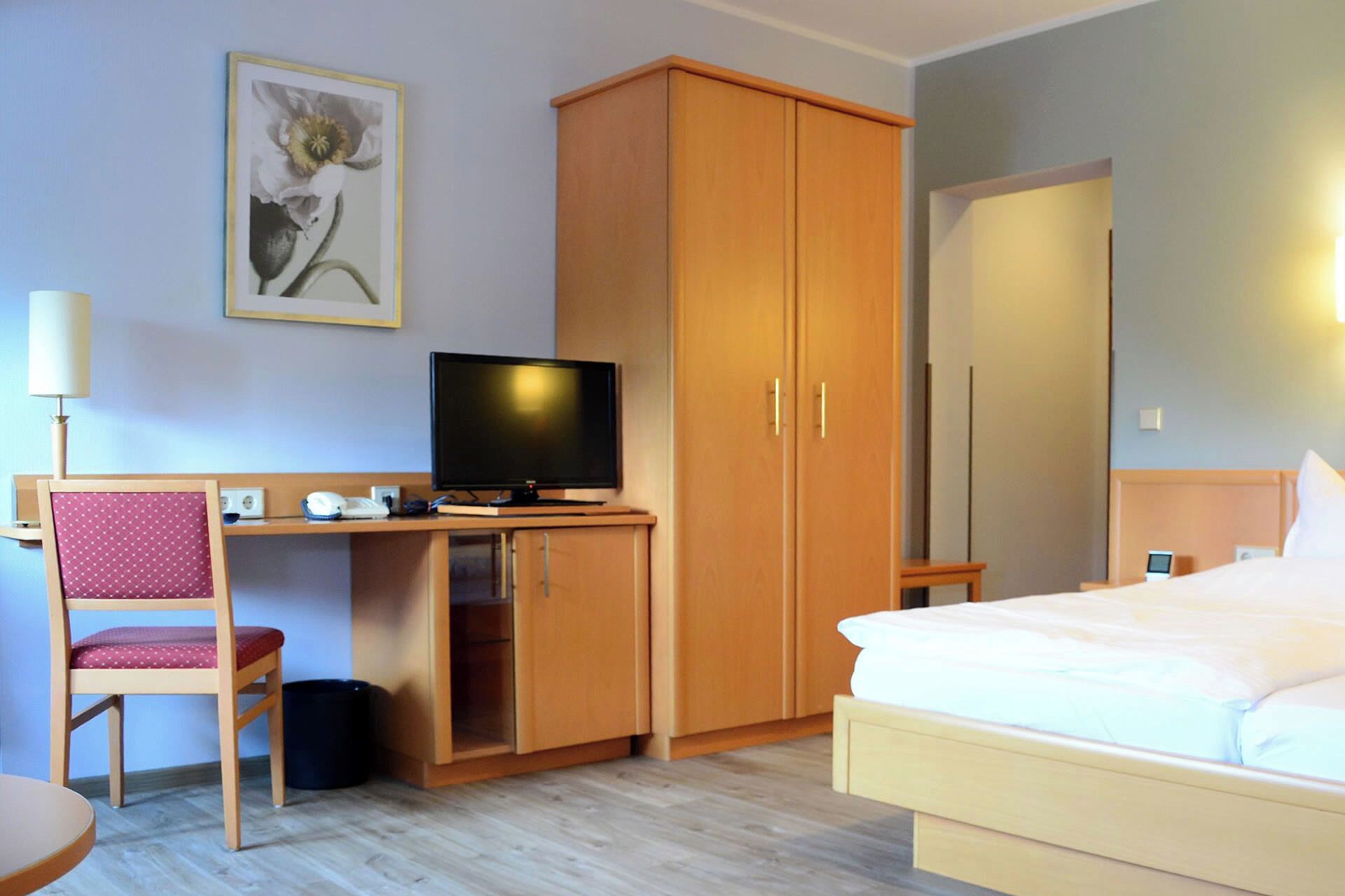Habitación de hotel con cama, escritorio con computadora, televisor, armario y una silla.