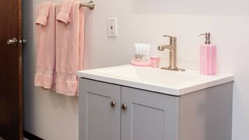 A bathroom with a grey cabinet, a white sink, and a mirror above it. There are pink towels hanging on a towel rack.