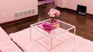 Ett rum med rosa tema, med ett soffbord av klart glas, en rosa soffa och en rosa matta.