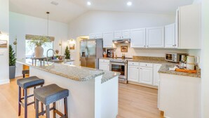 A modern kitchen with white cabinets, granite countertops, and stainless steel appliances. There are two bar stools and a large island with a sink. - Near Parks & Lakes: Sorrento Home w/ Pool & Yard! (Sorrento)