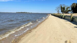 En strand med en träpromenad längs vattenbrynet, en sandstrand och gles vegetation.