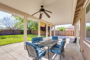 Eine überdachte Terrasse mit Tisch und Stühlen, einem Deckenventilator und Blick auf den Garten.