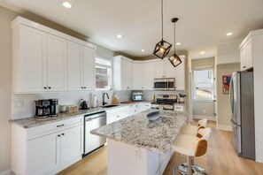 Una cocina moderna con armarios blancos, encimera de granito, horno empotrado y refrigerador de acero inoxidable.