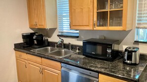 A kitchen with wooden cabinets, a double sink, a coffee maker, a microwave, a toaster, and a dishwasher.