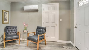 Ein Zimmer mit zwei schwarzen Ledersesseln, einem kleinen Tisch mit Blumen, einer weißen Tür und einer Klimaanlage an der Wand.