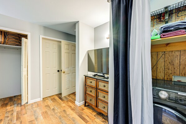 A room with a wooden floor, a white door, a wooden dresser, and a washing machine.