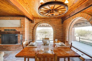 Un comedor con chimenea de ladrillo, techo de madera y ventanas arqueadas que dan a un paisaje.