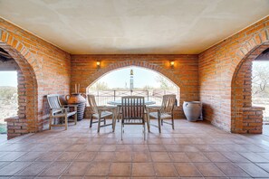 Un patio techado con un arco de ladrillo, una mesa redonda y cuatro sillas.