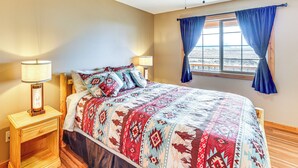 Un dormitorio con una cama, dos lámparas de noche, un ventilador de techo y una ventana con cortinas.