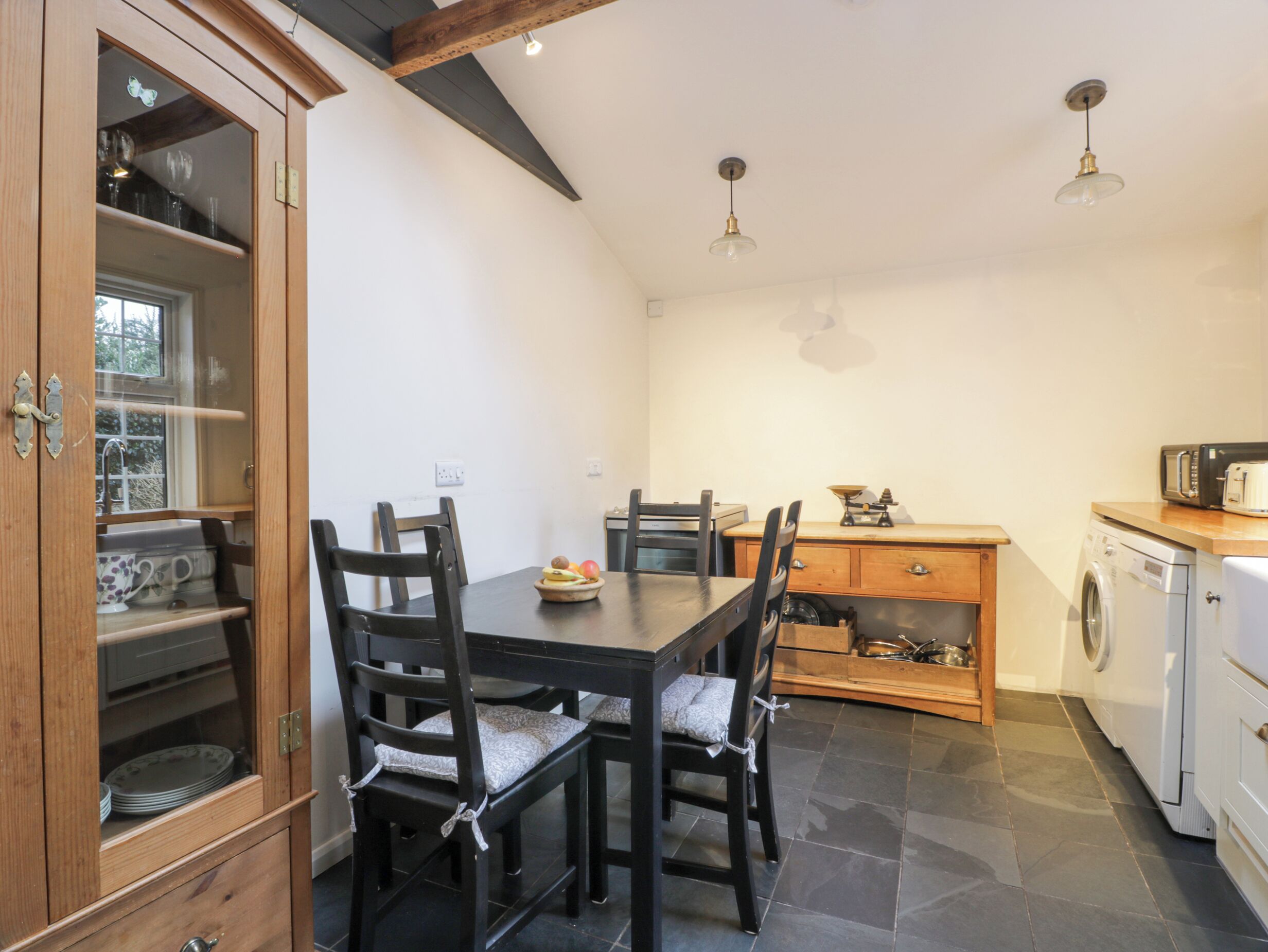 A compact kitchen with a dining table, chairs, a wooden cabinet, a washing machine, and a small window.