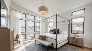 Ein modernes Schlafzimmer mit Himmelbett, einer Bank, einem Nachttisch und Blick auf eine verschneite Landschaft durch große Fenster.