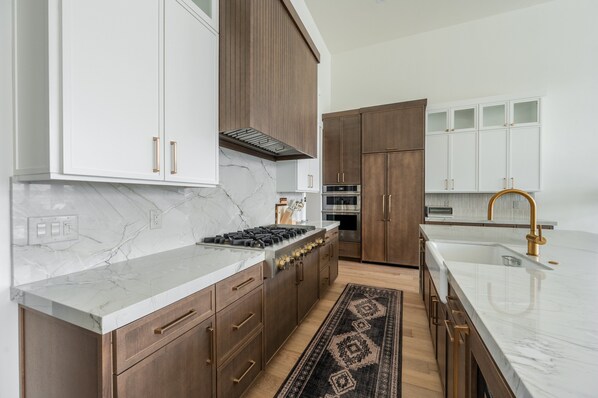 A modern kitchen with marble countertops, wooden cabinets, a gas stove, and a stainless steel oven. - Amanti Lago by Luxury Mountain (Heber City)