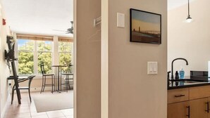 Eine moderne Küche mit schwarzem Arbeitsplatz, Spüle und Deckenventilator. Ein Essbereich mit Stühlen und Tisch sowie ein Fenster mit Blick auf Bäume.