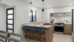 A modern kitchen with a central island, bar stools, a stove, and a refrigerator.