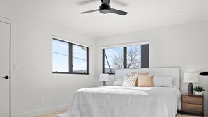 A bedroom with a bed, two bedside tables, a ceiling fan, and two windows.