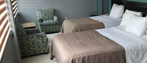 A hotel room with two beds, a small desk, and a patterned armchair.