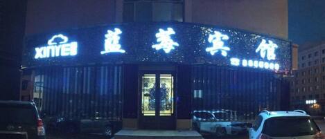 A building with illuminated signage, a staircase leading to the entrance, and parked cars in front.
