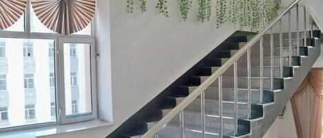 A staircase with a metal railing, a window with blinds, and hanging plants.