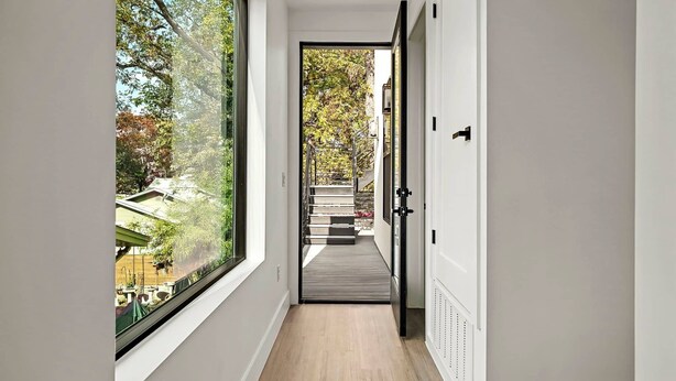 A narrow hallway with a large window on one side, leading to a staircase and a door on the other. - The West Twin Oasis - Hot Tub near Downtown Austin (Austin)