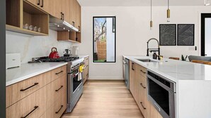 A modern kitchen with wooden cabinets, stainless steel appliances, and a large window. - The West Twin Oasis - Hot Tub near Downtown Austin (Austin)