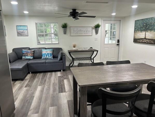 A modern living room with a gray sectional sofa, a wooden dining table, and a ceiling fan.