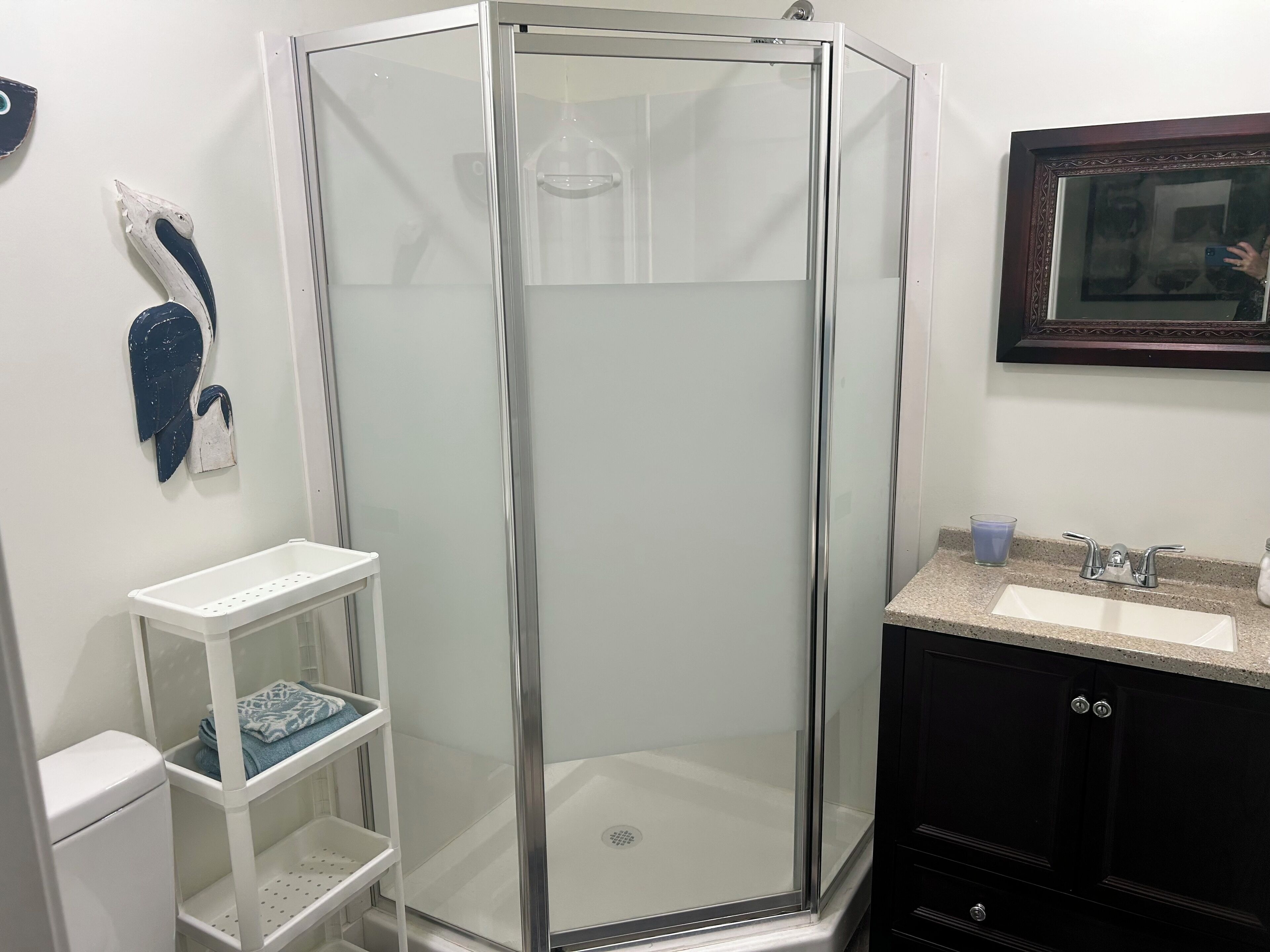 A bathroom with a glass-enclosed shower, a white sink, and a small shelf with towels.