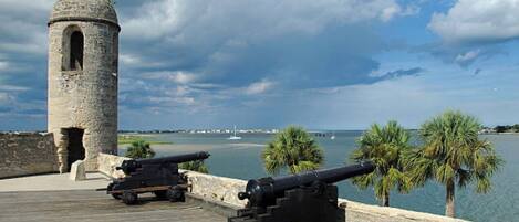 A coastal fort with cannons, a stone tower, and a wooden walkway overlooking the sea.