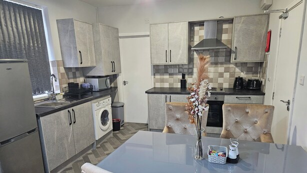 A modern kitchen with a built-in washing machine, a dining table with chairs, and a decorative vase.