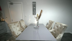 A dining area with a rectangular table, four upholstered chairs, and a vase with dried flowers.