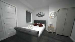 A bedroom with a bed, a nightstand, a lamp, a wardrobe, and a decorative mirror.
