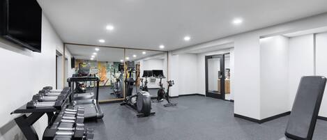A gym with exercise equipment, a mirror, and a door leading to another room.