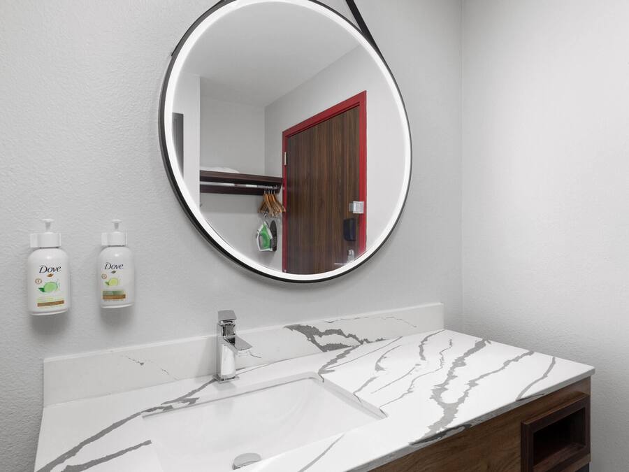 A bathroom with a white marble sink, a round mirror, and two Dove hand soap bottles.