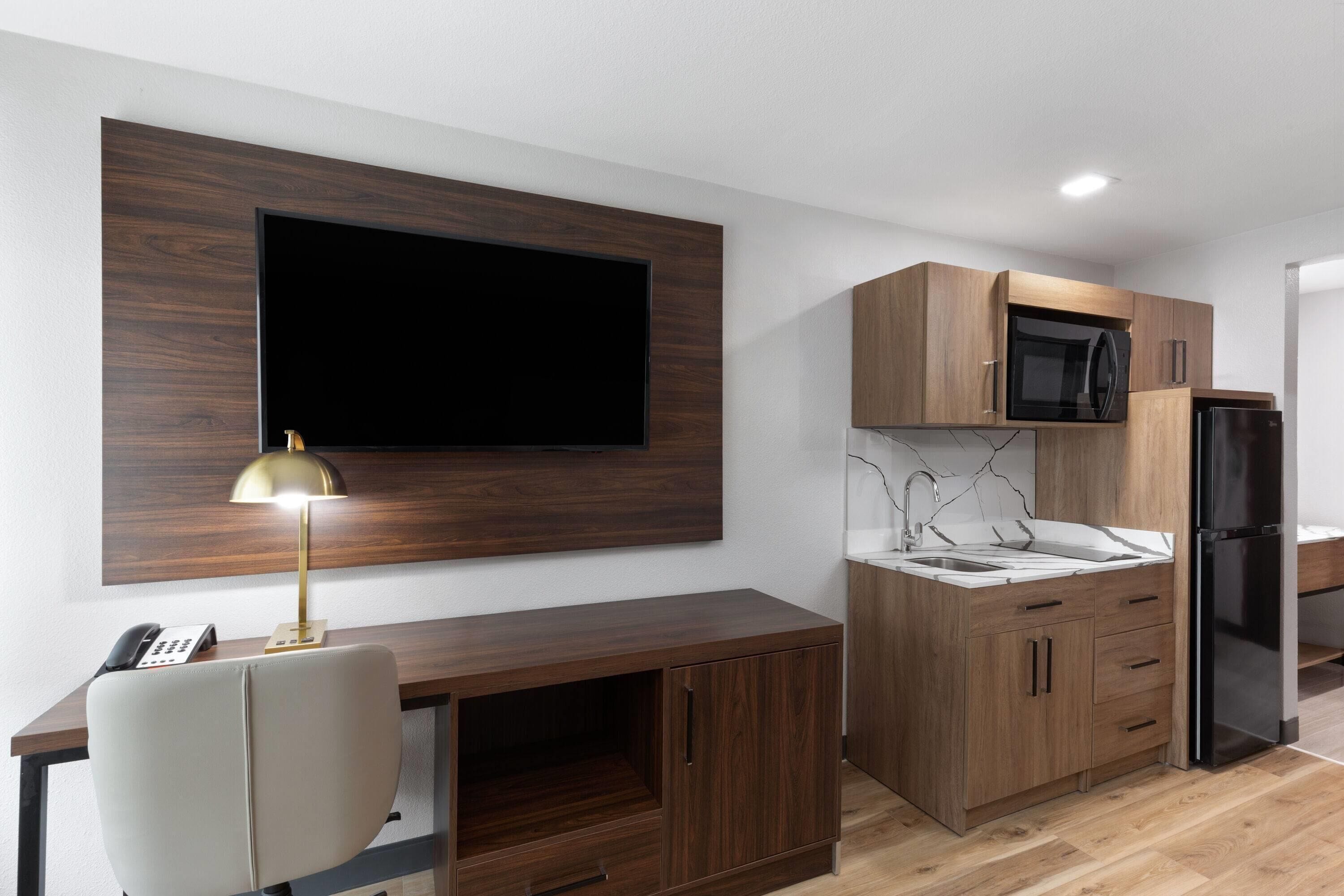 A modern kitchen with a built-in microwave, a refrigerator, and a wooden cabinet.
