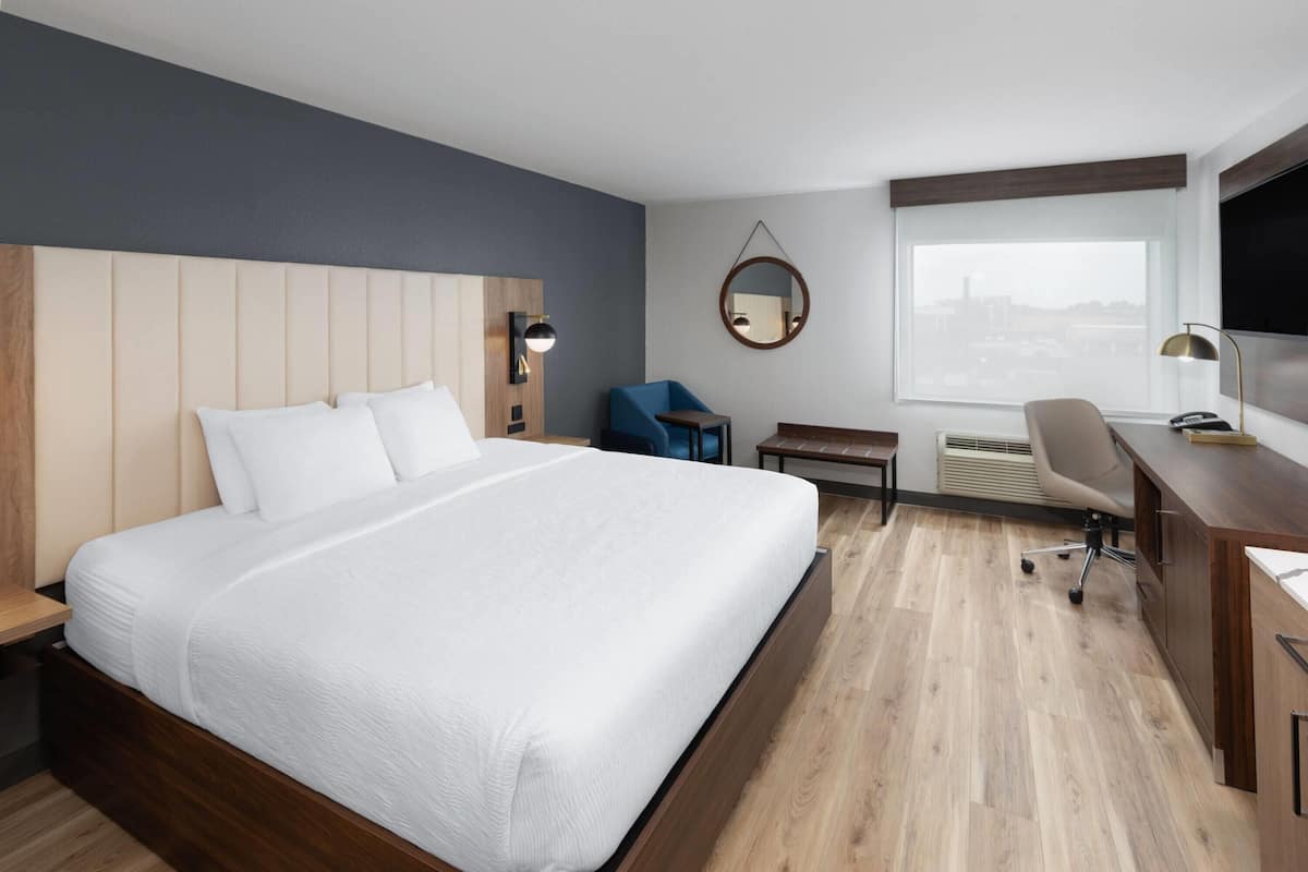 Une chambre d’hôtel moderne avec un grand lit, un bureau, une chaise, une petite table et un miroir.