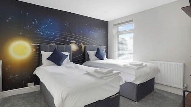 Una habitación de hotel con dos camas, un ventanal grande y un mural en la pared con un cielo estrellado.