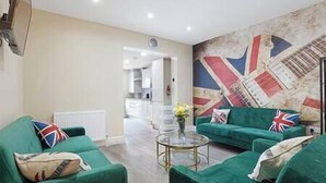 Una sala de estar con sofás verdes, una mesa de centro de cristal y un mural con diseño de la bandera del Reino Unido.