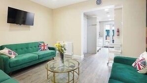 Una sala de estar con un sofá verde, una mesa de centro de vidrio y un televisor de pantalla plana montado en la pared.