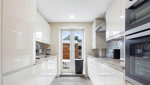 Una cocina moderna con armarios blancos, horno integrado y vistas al exterior a través de una puerta.