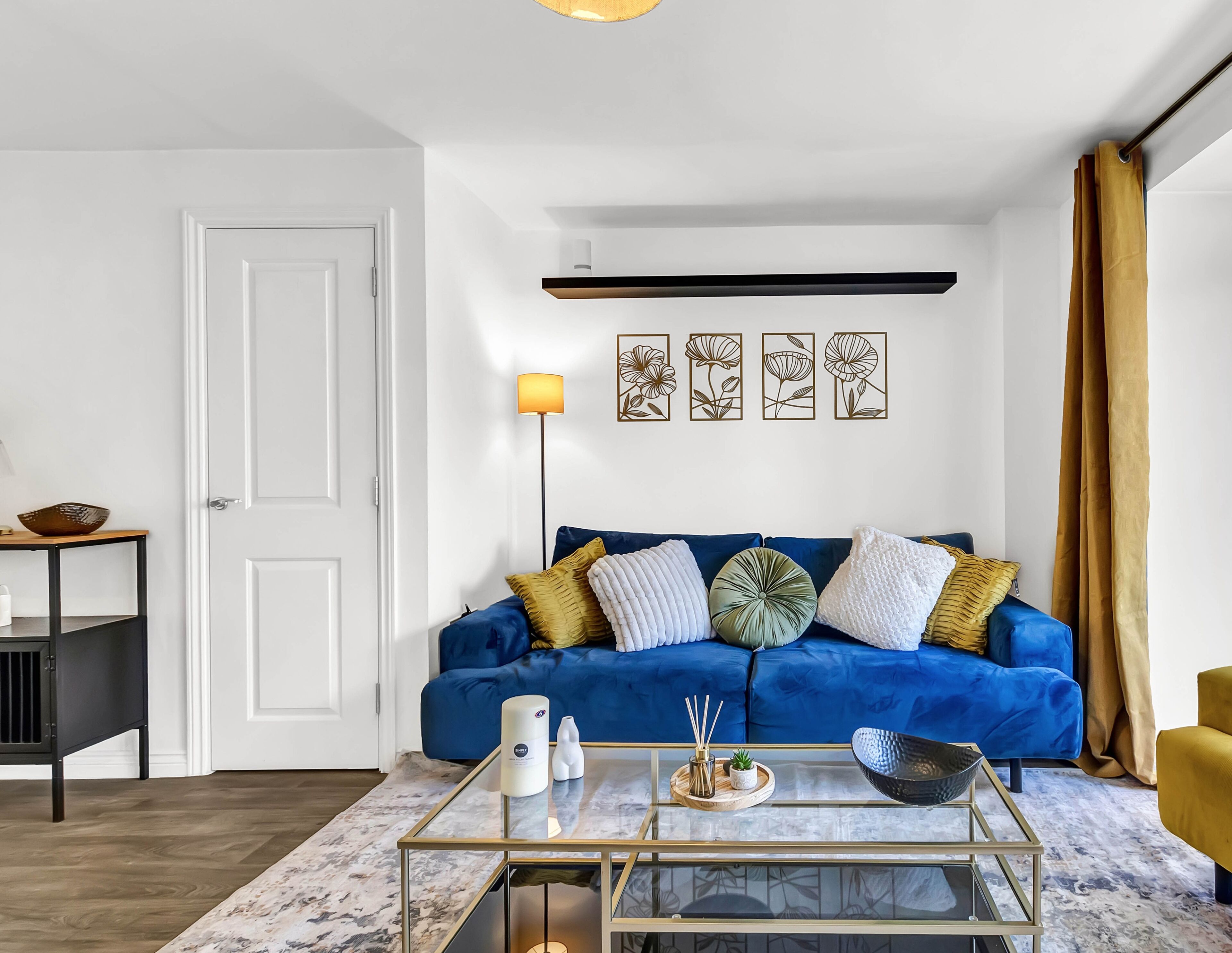 Ein Wohnzimmer mit einem blauen Sofa, einem Glastisch und einer Stehlampe.