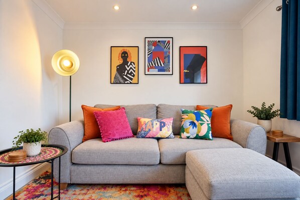 A living room with a grey sofa, colorful pillows, a small side table with a plant, and abstract art on the wall. - Stylish 2-Bed Bromley Apartment Short Walk to Town Centre, Spacious 2 Bedroom Flat Greater London (Bromley)