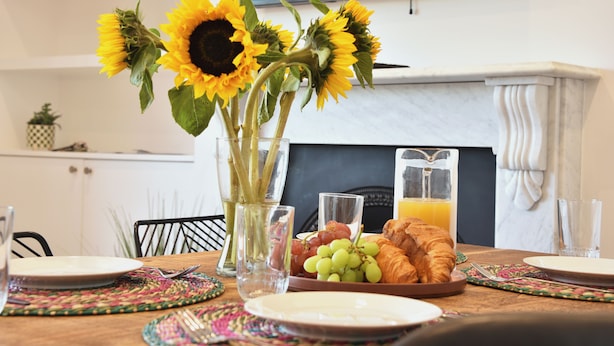 A breakfast table with a vase of sunflowers, a plate of croissants, grapes, and a glass of orange juice. - The Grove BR1, Spacious 2 Bedroom Flat Greater London (Bromley)