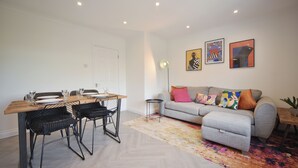 A modern living room with a dining area, featuring a sofa, a coffee table, and a dining table with chairs. - The Grove BR1, Spacious 2 Bedroom Flat Greater London (Bromley)