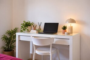 A white desk with a laptop, a lamp, and a potted plant.