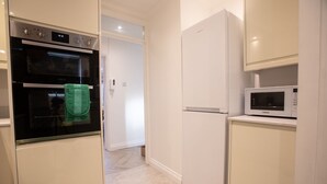 A compact kitchen with a built-in oven, a white refrigerator, and a microwave on the countertop. - The Grove BR1, Spacious 2 Bedroom Flat Greater London (Bromley)