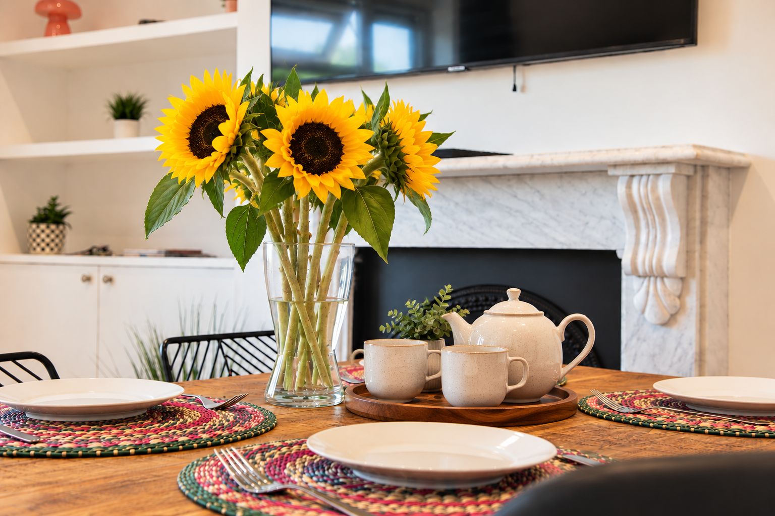 A dining table set with plates, a vase with sunflowers, a teapot, and cups.