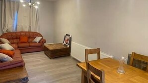 A living room with a brown leather sofa, a wooden coffee table, and a dining table with chairs. - Spacious & Cozy 3 Bedroom Home in Bexleyheath (Bexleyheath)