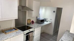 A compact kitchen with white cabinets, a built-in oven, a microwave, and a small countertop. - Spacious & Cozy 3 Bedroom Home in Bexleyheath (Bexleyheath)