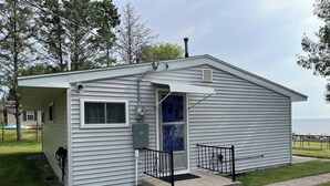 A small, single-story cabin with a covered porch, a door with a window, and a small outdoor area with a bench.